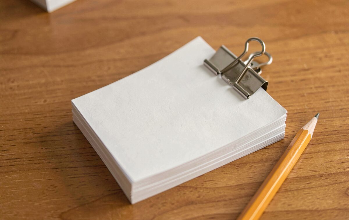 Blank index cards clipped together on a wooden desk, a pencil beside them